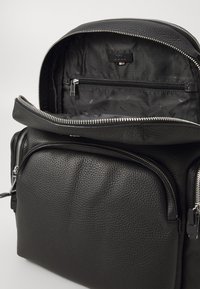 Black leather backpack featuring a textured finish, dual zippered compartments, and a branded interior lining with additional zip pocket.
