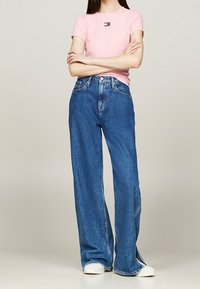 Light pink short-sleeve top with logo; high-waisted blue wide-leg jeans; white sneakers. Jeans feature a frayed hem and side slits.