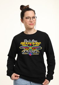 Felpa nera con una grafica colorata che presenta la scritta "Don't Stop Believin'" e un'immagine stilizzata di un uccello in colori vivaci.