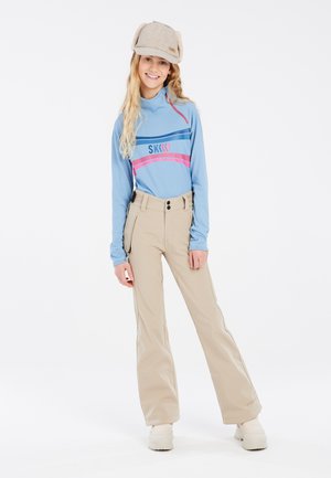 Camicia azzurra a maniche lunghe con motivo a righe e pantaloni da neve beige con due tasche frontali e dettaglio in vita con doppio bottone. Stivali da neve bianchi.