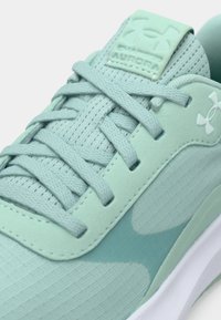 Κοντινό πλάνο αθλητικού παπουτσιού Under Armour σε μέντα πράσινο χρώμα με υφασμάτινη υφή, κορδόνια στο ίδιο χρώμα και λογότυπο στο πλάι και στη γλώσσα του παπουτσιού.