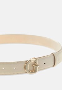 Beżowy skórzany pasek o gładkiej fakturze, z metalową złotą klamrą w kształcie litery G oraz kilkoma dziurkami do regulacji na pasku.