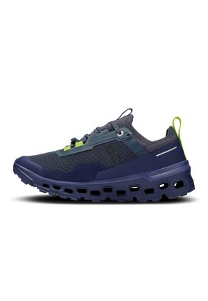 Dark blue and gray athletic shoe with mesh upper, thick rugged sole with cutouts, lime green pull tab, and lace-up design.
