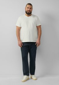 Witte katoenen t-shirt gecombineerd met marineblauwe broek en crème sneakers. Eenvoudig ontwerp, korte mouwen en een relaxte pasvorm. Geen zichtbare patronen of accenten.