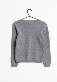 Maglione grigio lavorato a maglia appeso a una gruccia nera, caratterizzato da un collo rotondo e un motivo a punti testurizzati su tutto il tessuto.