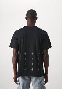 Černé bavlněné tričko s kulatým výstřihem, krátkými rukávy a grafikou světle šedých křížů na zadní straně. Pohodlný střih a minimalistický design.