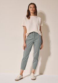 Top in maglia a trama fine di colore crema chiaro, abbinato a pantaloni grigi chiari a sigaretta e sneakers beige. I pantaloni presentano tasche anteriori e una chiusura a bottone.