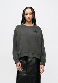 Σκούρο πράσινο φούτερ με χαλαρή εφαρμογή και στρογγυλή λαιμόκοψη, με κεντημένο κείμενο "DANCE STUDIO BOSS" στο στήθος.