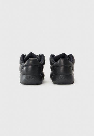 Zwarte sneakers met een gladde textuur, ronde vorm en gewatteerde enkelsupport. Heeft subtiele merkvermelding op de hiel.