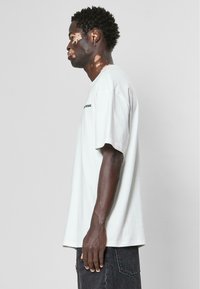 Tricou oversized gri deschis cu mânecile scurte, având un guler rotund și text imprimat pe piept. Asortat cu șorturi din denim închis.