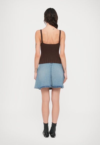 Καφέ ριμπ πλεκτό τοπ με λεπτές τιράντες, συνδυασμένο με μια μίνι φούστα από ανοιχτό μπλε τζιν με ξεφτισμένο τελείωμα. Μαύρα παπούτσια και σκούρες κάλτσες.