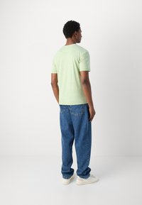 Cămașă scurtă, de culoare verde deschis, confecționată dintr-un material moale, asortată cu blugi lejeri din denim albastru. Outfitul este completat cu adidași albi.
