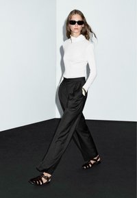 White long-sleeve top, black pleated trousers, and dark sandals. Smooth fabric, fitted silhouette, and contrasting textures. Minimalist style.