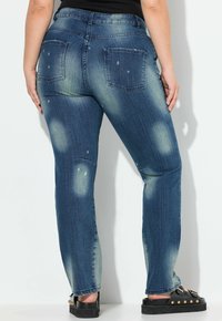 Jeans in denim con una tonalità azzurra sbiadita e dettagli strappati, gamba dritta e due tasche posteriori, abbinati a sandali con plateau neri.