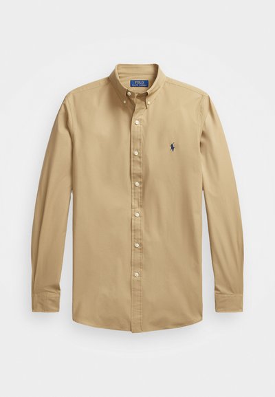 Lys beige langermet skjorte med knapper laget av glatt bomull. Har en spiss krage og en liten blå brodert hestelogo på brystet.