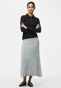 Camisa polo de manga larga de color negro con canalé y cuello, combinada con una falda larga de punto gris, que presenta un corte recto y una textura sutil. Bailarinas negras.