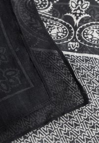 Juodai baltas raštuotas šalikas, kuriame vaizduojami sudėtingi paisley ir geometriniai raštai, turintis permatomą tekstūrą ir siuvinėtus kraštus.