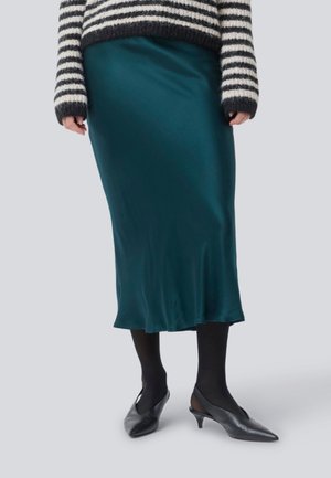 Teal satijnen midi-rok met een gladde textuur, gecombineerd met zwarte panty’s en puntige hakken. Wol gestreepte trui erboven.