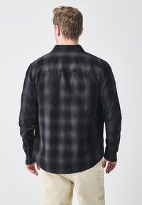Zwarte geruite flanellen shirt met een knoopsluiting-kraag, lange mouwen en een afgeronde zoom, met een gladde textuur en subtiele schaduwwerking.