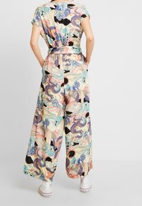 Woman wearing pastel-colored wide-leg pants and matching short-sleeve top with dragon and wave patterns, paired with white high-top sneakers.