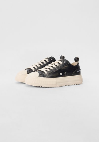 Schwarze Sneaker mit einer Gummikappe an der Zehe, cremefarbenen Schnürsenkeln und einer strukturierten Sohle. Verfügt über kontrastierende Akzente und eine Schlaufe an der Ferse.
