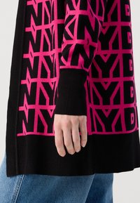 Melnā džemperī ar rozā ģeometrisko "NY" modeli. Piedurkņu un apakšmalas ribotais dizains izceļ gludo adījuma tekstūru un piegulošo siluetu.