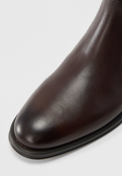 Brauner Leder-Stiefelette mit glatter Oberfläche, abgerundeter Spitze und dünner schwarzer Sohle. Dezente Nahtdetails am Rand.