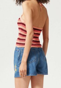 Donna che indossa un top senza maniche a righe rosa e bordeaux insieme a pantaloni corti in denim blu con ricami floreali sul lato sinistro.