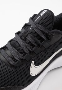 Schwarzer Sportschuh mit Mesh-Material, flachen Schnürsenkeln und weißem Nike Swoosh-Logo. Verfügt über eine strukturierte Oberfläche und eine gepolsterte Sohle.