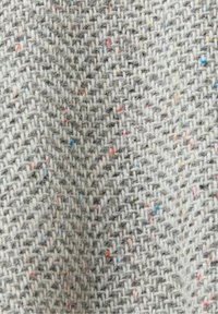 Gros plan sur un tissu en laine gris à chevrons avec des éclats colorés en rouge, bleu, jaune et orange tissés à travers.