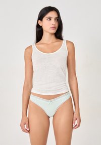 Un débardeur blanc et un string à dentelle vert menthe. Le string présente un petit détail en forme de nœud à l'avant, soulignant son design délicat.