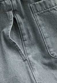 Denimtyg i en ljusgrå nyans, med en sidoficka som har en ren, något texturerad yta och subtila blekningar för visuell intresse.