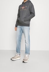 Felpa grigia con logo, tasca a marsupio e polsini a coste. Jeans azzurri chiari con vestibilità comoda e orli risvoltati. Sneakers chiare.
