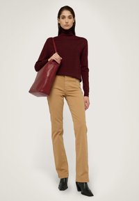 Suéter de cuello alto burdeos, pantalones color beige y botas negras de tacón. Bolsa tote de cuero rojo con textura suave y detalles mínimos en hardware.