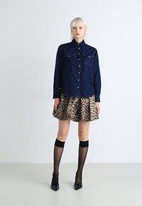 Tmavomodrá džínsová košeľa na gombíky s dvoma náprsními vreckami, skombinovaná s leopardím zvieracím vzorom v bufante. Modelka má na sebe čierne wysoké ponožky a vysoké opätky.