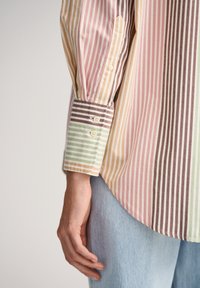Chemise rayée avec plusieurs couleurs : rose, vert, marron, beige, avec des poignets à bouton et un tissu doux. Design décontracté avec une coupe ample.