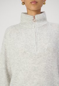 Light gray knit pullover with a high collar and half-zip closure. Features a textured, ribbed pattern and a rectangular patch pocket.