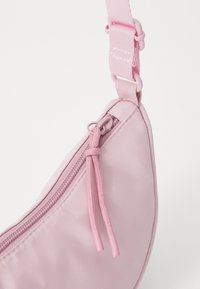 Rosa nylon sling-perse med glidelås, rund form, teksturert stoff og justerbar stropp. Merkelig snor detalj ved glidelåsen.