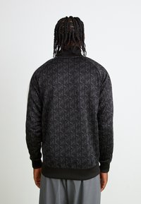 Zwarte sweatshirt met een herhalend logo-patroon, geribde manchetten en zoom, en een hoge kraag. Zachte textuur, casual pasvorm.