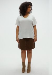 Λευκό, υφασμάτινο τοπ με λαιμόκοψη σε σχήμα V, συνδυασμένο με καφέ φούστα με κουμπιά μπροστά. Το μοντέλο φοράει μπεζ μπότες αστραγάλου, παρουσιάζοντας μια άνετη γραμμή και σχεδιασμό με στρώσεις.