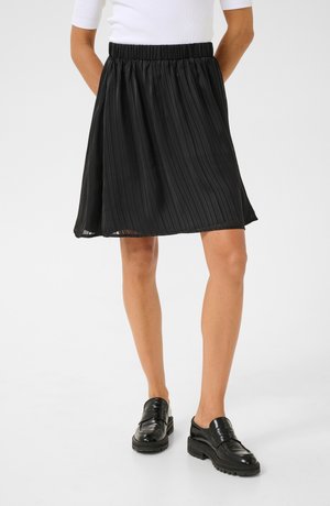 Jupe plissée noire avec une taille élastique, présentant une texture soyeuse et un design fluide, associée à des mocassins noirs brillants.