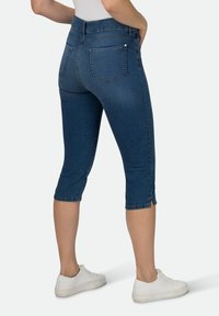 Dunkelblaue Denim-Capri-Jeans mit mittelhoher Taille, verkürzter Länge, Gesäßtaschen und dezenten seitlichen Schlitzen am Saum. Stylisch mit weißen Sneakers kombiniert.