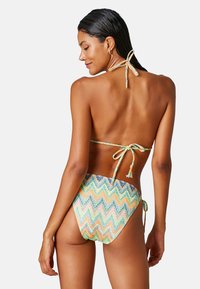 Bikini w wielokolorowym wzorze w zygzaki, z wiązaniami na szyi i plecach, wykonany z gładkiego materiału. Posiada wysokie wycięcie z tyłu oraz minimalne krycie.