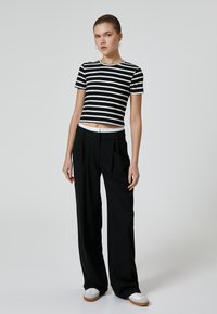 Top corto a rayas en blanco y negro, con mangas cortas y cuello redondo, combinado con pantalones anchos negros y zapatillas blancas. Diseño minimalista.