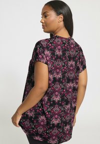 Czarna bluzka z krótkim rękawem z różowo-białym wzorem kwiatowym, w luźnym fasonie, okrągłym dekoltem i subtelnymi fałdami z tyłu.