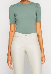 Grön åtsittande topp med korta puffärmar, tillsammans med ljusbeige skinny jeans med knappknäppning och fina sömdetaljer.