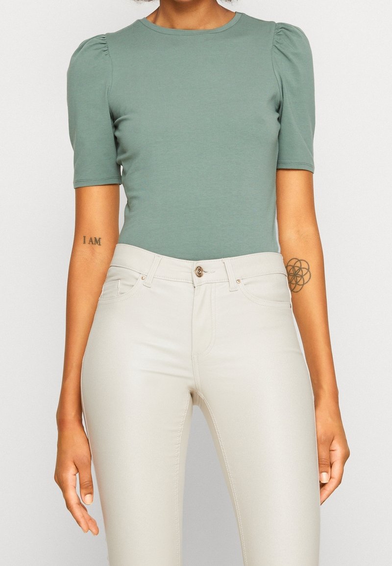 Grön åtsittande topp med korta puffärmar, tillsammans med ljusbeige skinny jeans med knappknäppning och fina sömdetaljer.