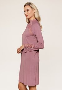 Robe mauve à manches longues avec des accents en dentelle au niveau de l'encolure et des manches. Tissu doux, silhouette légèrement évasée, ourlet à hauteur du genou.