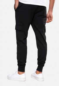 Zwarte cargo joggers gemaakt van zachte stof, met zijzakken en elastische boorden, gecombineerd met witte sneakers.
