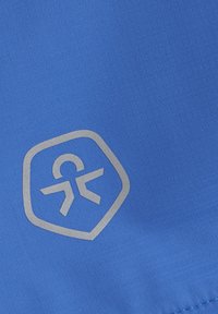 Blått tyg med ett texturerat mönster, prytt med en silverfärgad logotyp i hexagonal form. Designen är stilren och modern.